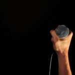 Close-up of a hand firmly gripping a microphone against a dark backdrop.