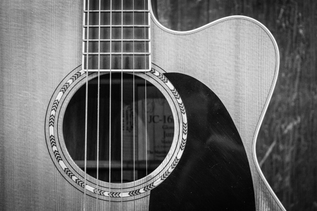 Detailed black and white photo of an acoustic guitar showcasing strings and sound hole.