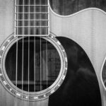 Detailed black and white photo of an acoustic guitar showcasing strings and sound hole.