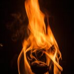 Dramatic close-up of vibrant fire flames and burning wood against a dark background.