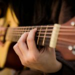 Close view of fingers strumming an acoustic guitar, capturing the essence of music creation.