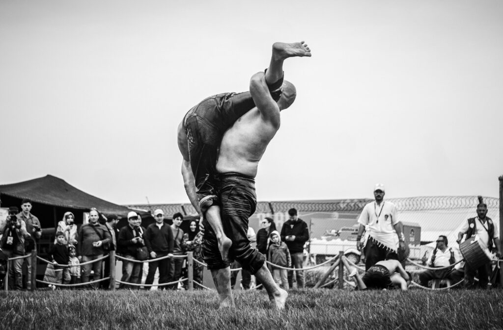 Black and white photo of an intense outdoor wrestling match with an audience in the background.