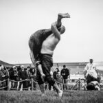 Black and white photo of an intense outdoor wrestling match with an audience in the background.