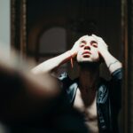Man with tattoos reflects on inner struggle in moody indoor portrait.