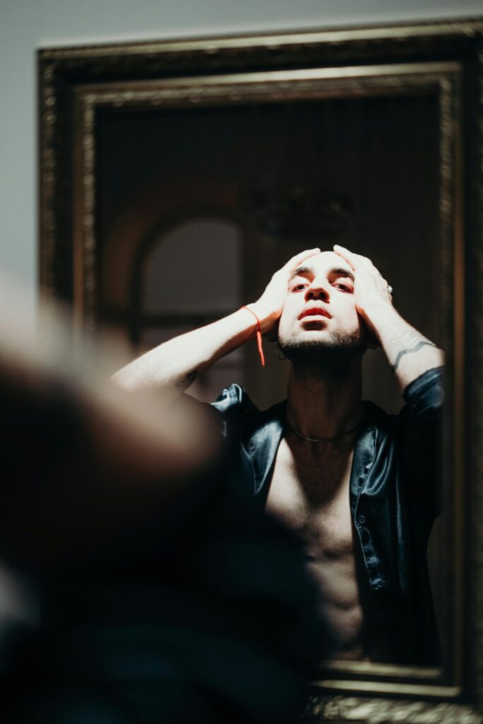 Man with tattoos reflects on inner struggle in moody indoor portrait.