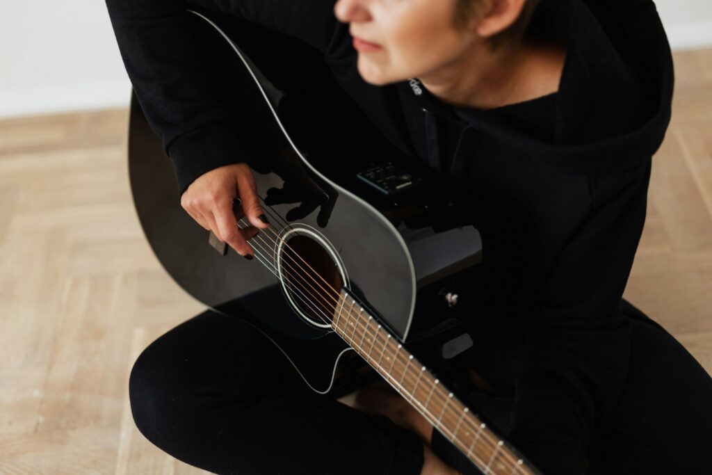 Person playing an acoustic guitar indoors, focusing on strings and hands.