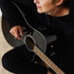 Person playing an acoustic guitar indoors, focusing on strings and hands.