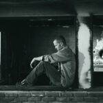 A young man sits pensively in a derelict building, embodying solitude and contemplation.