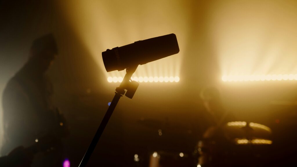 Silhouette of a microphone with musicians performing on a dimly lit stage.