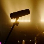 Silhouette of a microphone with musicians performing on a dimly lit stage.