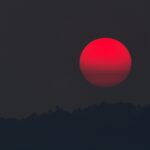 A captivating blood moon rising over a silhouette of hills, capturing the beauty of twilight.
