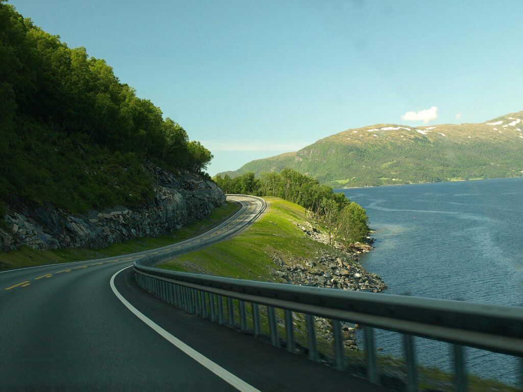 Breathtaking view of a winding road along a Norwegian fjord, surrounded by water and lush greenery.