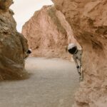 Astronauts peek from behind rocks in a fantasy extraterrestrial landscape.