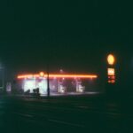 A foggy night scene of an illuminated gas station, featuring vibrant neon lights.