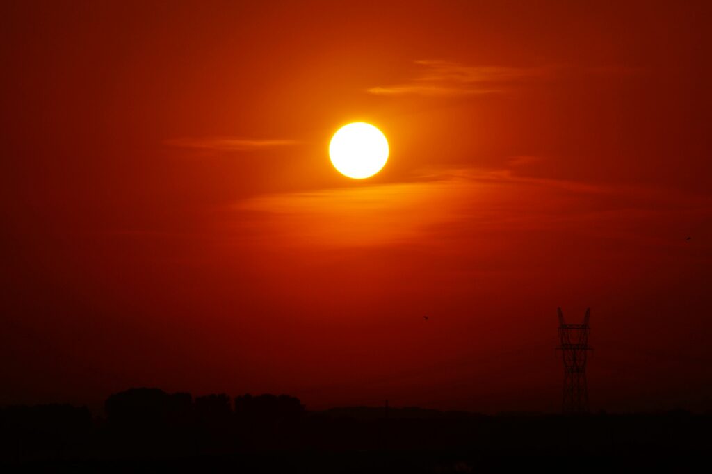 A striking sunset casting a golden glow over a silhouetted landscape with a power line tower.