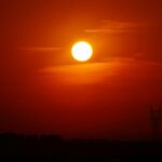 A striking sunset casting a golden glow over a silhouetted landscape with a power line tower.