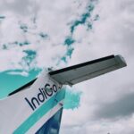 View of an airplane tail against a bright sky filled with clouds, showcasing travel themes.