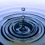 A stunning close-up of a water droplet creating ripples on a smooth water surface, capturing nature's simplicity.