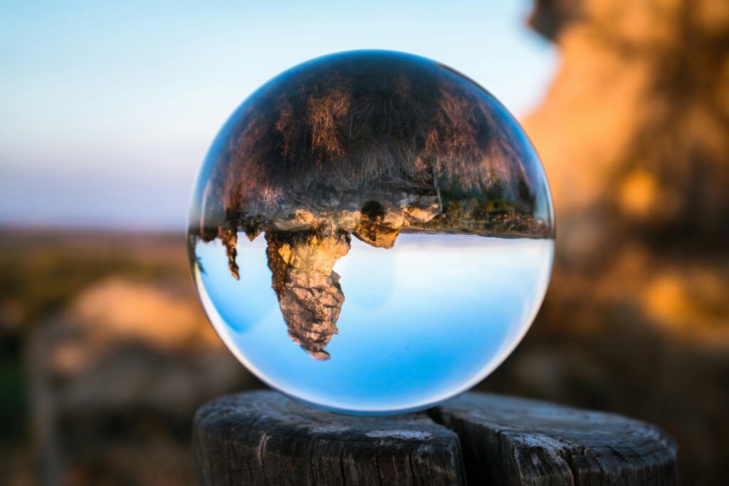 A crystal ball capturing an inverted landscape on a wooden stump in daylight.