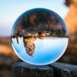 A crystal ball capturing an inverted landscape on a wooden stump in daylight.