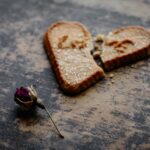 Broken heart-shaped cookie with a dry rose symbolizes love and heartbreak.