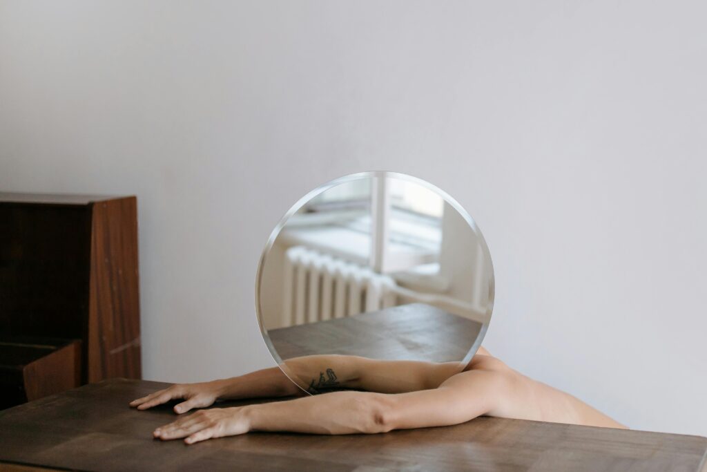 Artistic shot of arms holding a round mirror, reflecting a minimalist interior with wooden furnishings.