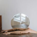 Artistic shot of arms holding a round mirror, reflecting a minimalist interior with wooden furnishings.