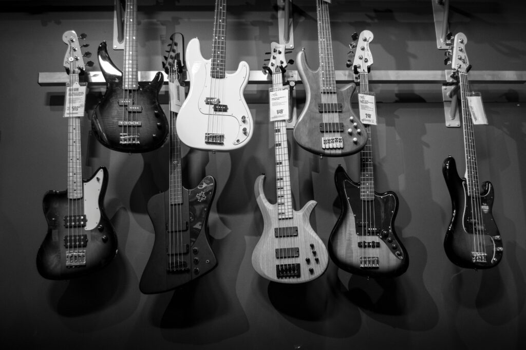 Black and white display of various electric bass guitars hanging on a rack.