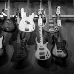 Black and white display of various electric bass guitars hanging on a rack.