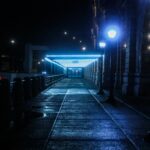 A moody, illuminated pathway at a train station during night with glowing lamps.